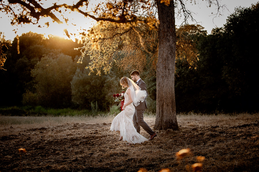 bride and groom walking through a field at sunset